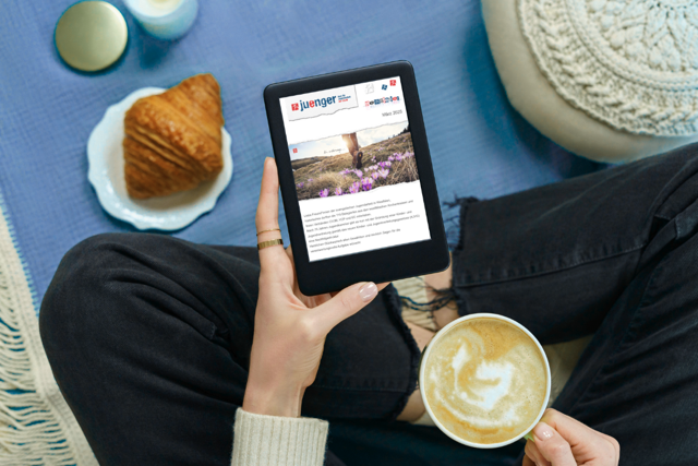 Person liest den juenger-Newsletter der Evangelischen Jugend von Westfalen gemütlich auf dem Tablet bei Kaffee und Croissant.