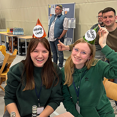 Zwei junge Frauen mit Partyhüten lächeln in die Kamera.