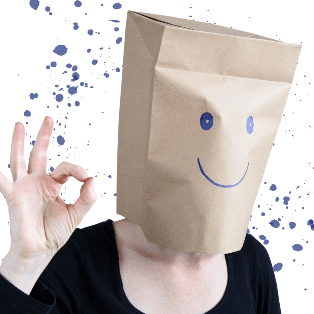 Person mit brauner Papiertüte über dem Kopf, darauf ein aufgemaltes Smiley-Gesicht, zeigt mit der Hand das OK-Zeichen.