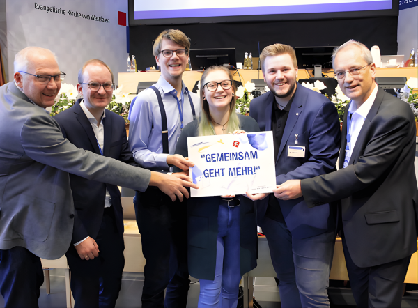 Sechs Personen halten ein Schild „Gemeinsam geht mehr!“ bei der Landessynode Veranstaltung der Evangelischen Kirche von Westfalen.