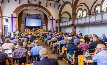 Synodensitzung der EKvW in Bielefeld Bethel: viele Delegierte sitzen in Reihen und blicken zur Bühne mit Leinwand.