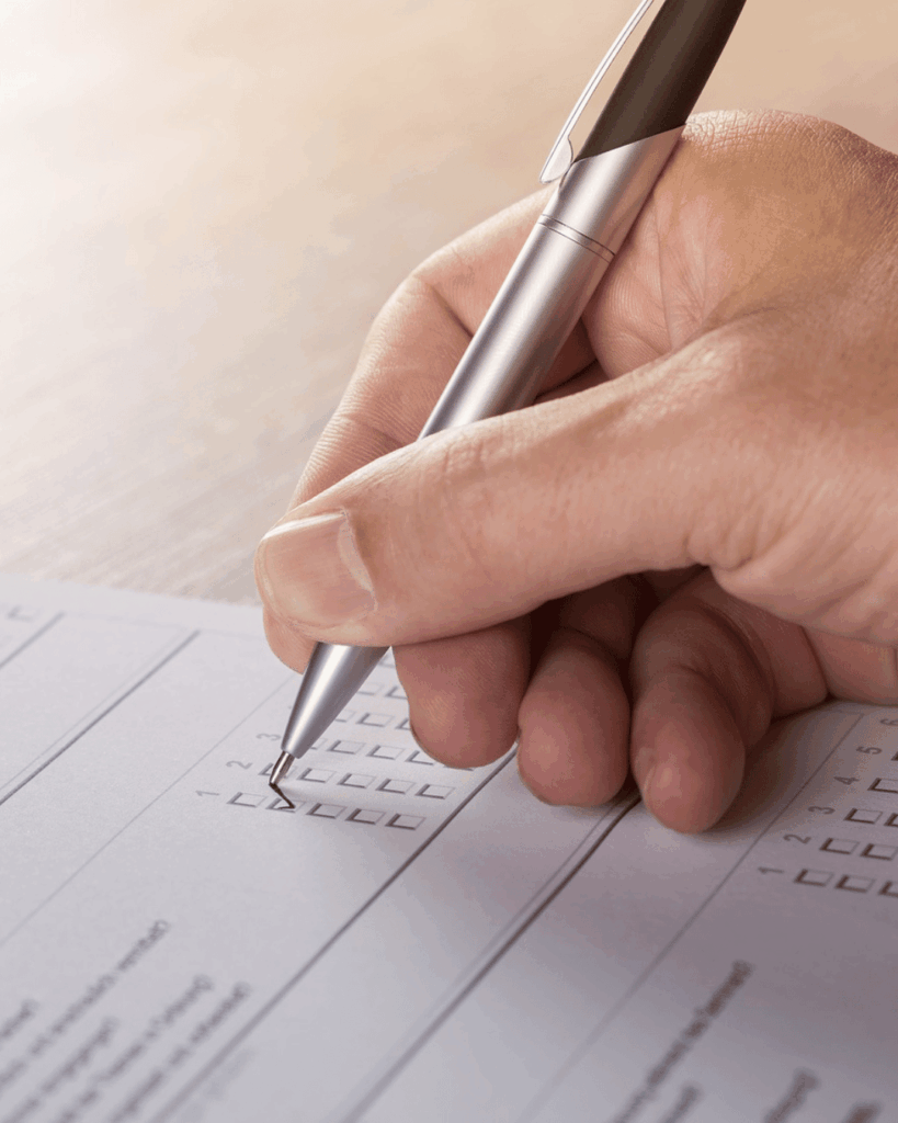 Hand hält einen Stift und setzt ein Häkchen in ein Formular mit Auswahlfeldern auf Papier.