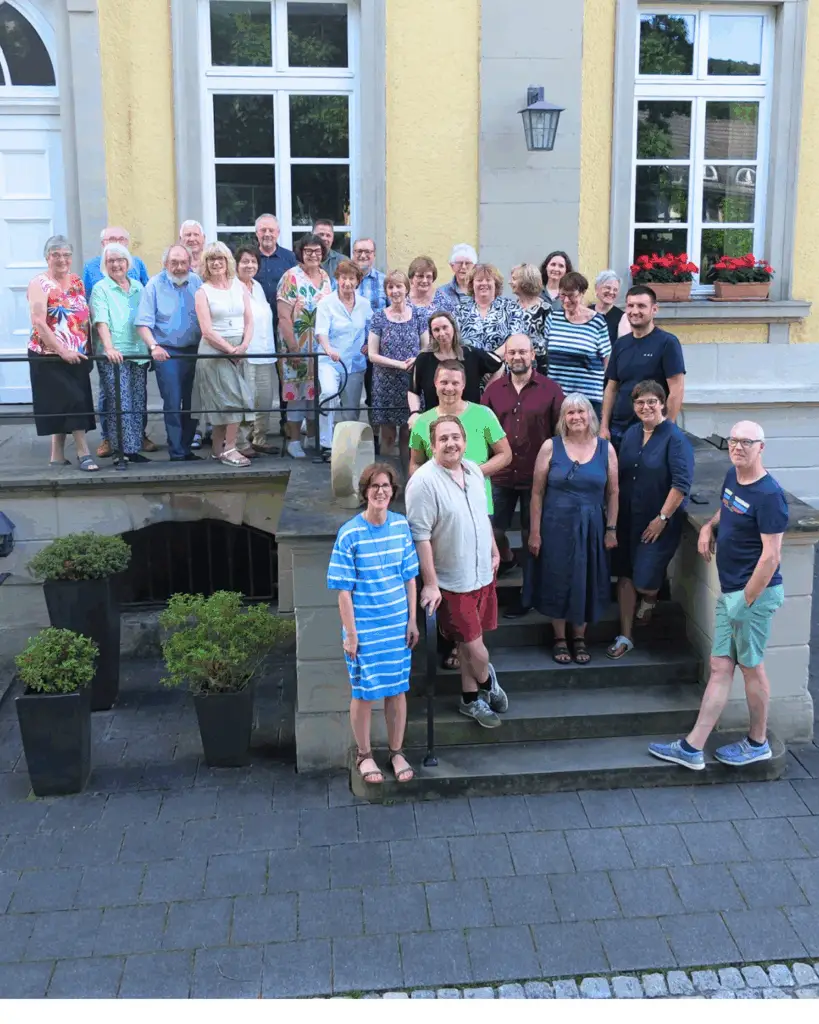 Gruppenfoto von Mitarbeitenden des Amtes für Jugendarbeit vor Haus Villigst bei sommerlichem Wetter.